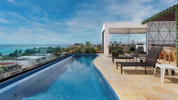 A rooftop infinity pool with a clear view of the ocean, lounge chairs, and a modern outdoor kitchen area. - Beautiful view Studio near Beach (Playa del Carmen)
