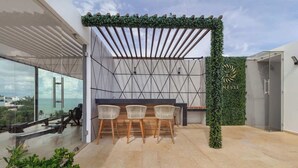 A rooftop terrace with a pergola, three wicker chairs, a glass table, and a wall with a sun logo. - Beautiful view Studio near Beach (Playa del Carmen)