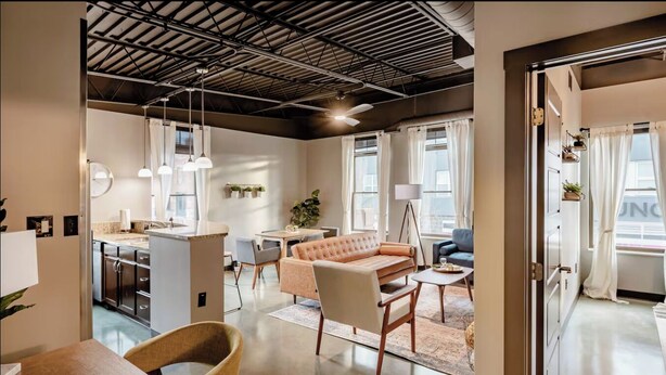 Een ruime woonkamer met een bank, een eettafel en een keuken op de achtergrond.