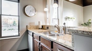 Een keuken met granieten aanrecht, een roestvrijstalen spoelbak, een vaatwasser en een klok aan de muur.