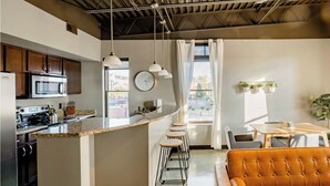Een moderne keuken met een centraal eiland, barkrukken, een eettafel met stoelen en een leren bank.