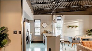 Een moderne keuken met een centraal eiland, een eethoek met tafel en stoelen, en een zithoek met een bank.