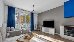Een moderne woonkamer met een bank, een bijzettafeltje met een taart, een televisie en een keukenhoek met een fornuis.