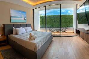 A modern bedroom with a large bed, a painting, a balcony with chairs, and a TV. - Beachside Studio & Jacuzzi Bliss (Playa del Carmen)