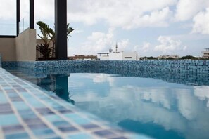 A swimming pool with blue mosaic tiles, surrounded by a low wall and some greenery. - Beachside Studio & Jacuzzi Bliss (Playa del Carmen)