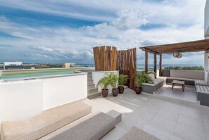 A rooftop terrace with a view of the ocean, a wooden pergola, and outdoor seating. - Stunning Ocean View Studio from your bed (Playa del Carmen)