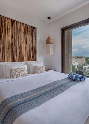 A hotel room with a large bed, a view of the city through a large window, a wooden wall panel, and a hanging light fixture. - Stunning Ocean View Studio from your bed (Playa del Carmen)