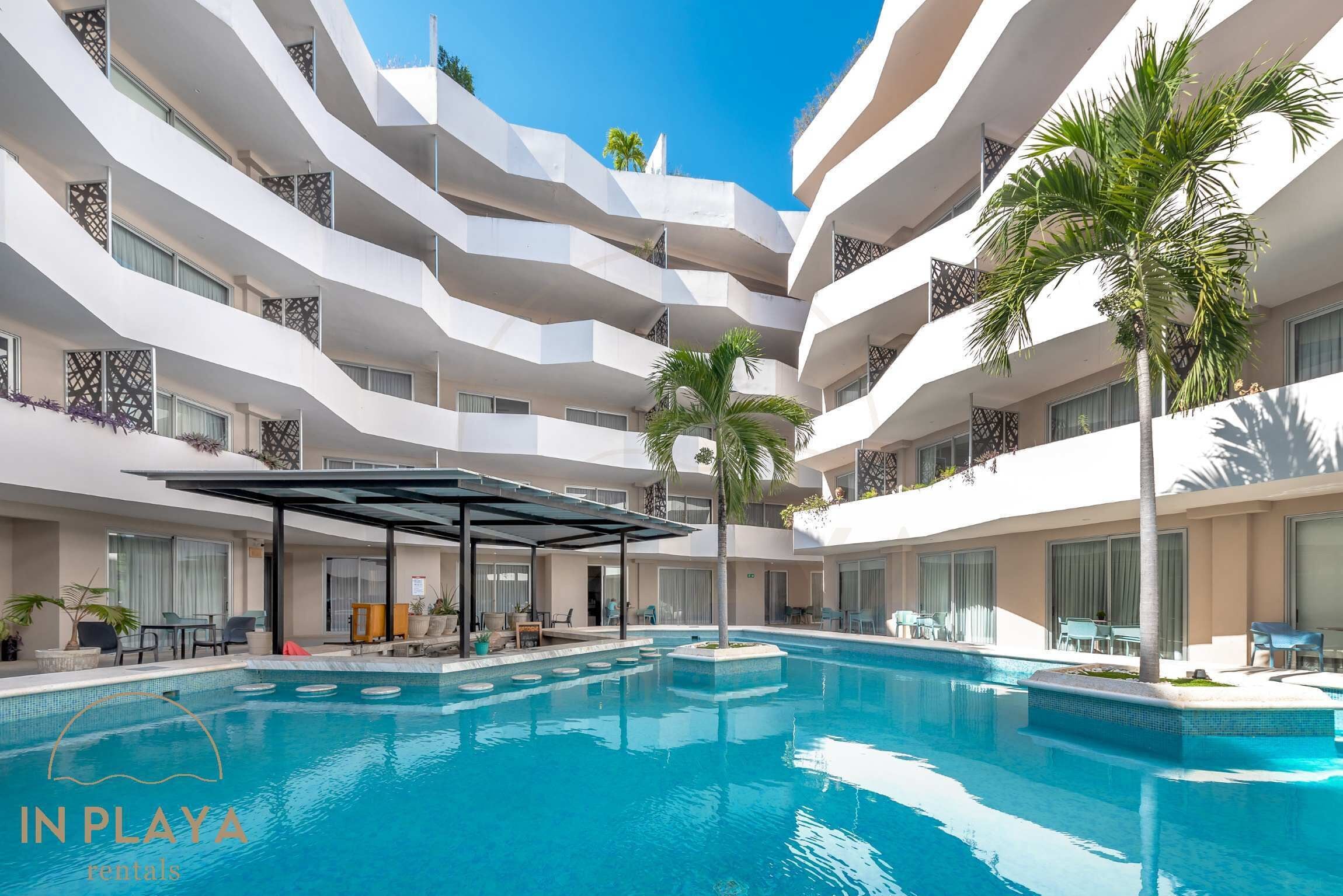 Ein mehrstöckiges Hotel mit einem zentralen Schwimmbecken, Balkonen mit Pflanzen und Außenbereichen zum Sitzen.