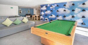 Een pooltafel in een moderne ruimte, met een blauwe wand waarop een motief van wolken en hoeden is afgebeeld.