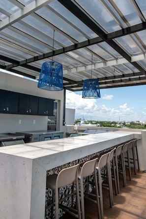 A modern kitchen with a large island, bar stools, and hanging blue pendant lights. - Stylish Condo Rooftop Views & 2 Pools Near 5th Ave (Playa del Carmen)