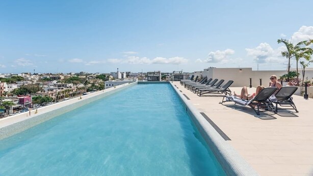 Une piscine sur le toit, dotée de chaises longues et offrant une vue sur le paysage urbain.