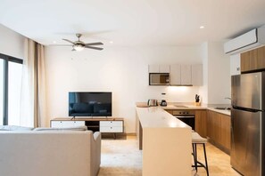 A modern kitchen with a built-in microwave, stove, and refrigerator. There is a dining area with a bar stool and a television in the background. - Spectacular Rooftop Pools, Steps to Beach and 5th Ave (Playa del Carmen)