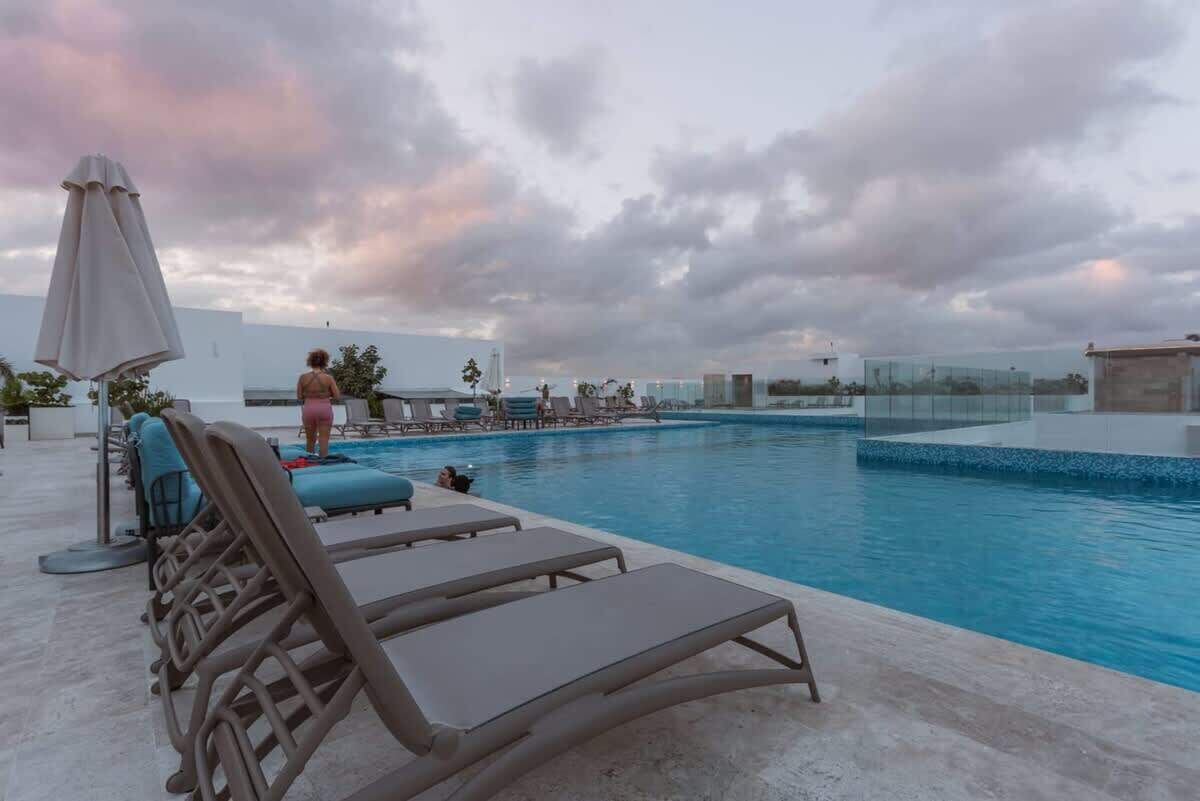 A swimming pool area with lounge chairs and a person walking by.