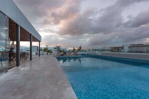 Une piscine sur le toit, au design moderne, entourée de chaises longues et d’un espace salon abrité.