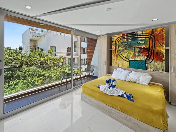 Een moderne hotelkamer met een groot bed, een balkon met uitzicht op groen en een eigentijds schilderij aan de muur.