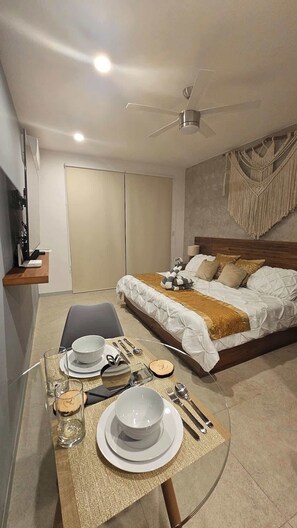 A bedroom with a bed, a desk with a chair, and a dining area with a table set for two. - Modern Studio w Pools & Gym Near 5th Ave (Playa del Carmen)