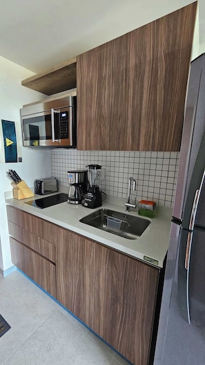A modern kitchen with wooden cabinets, a stainless steel refrigerator, a microwave, a toaster, a blender, and a sink. - Modern Studio w Pools & Gym Near 5th Ave (Playa del Carmen)