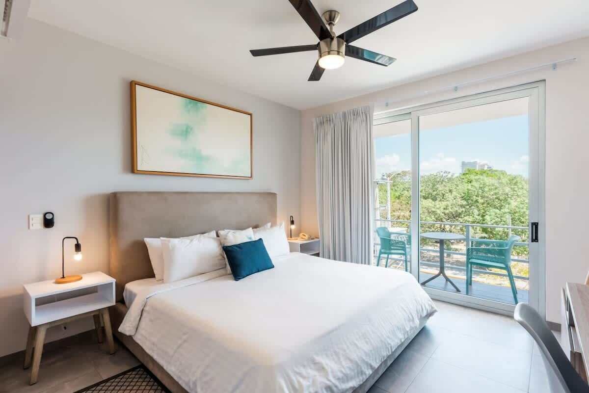 Une chambre d’hôtel avec un lit, un ventilateur de plafond, une table de chevet, une fenêtre avec des rideaux et une vue sur la verdure.