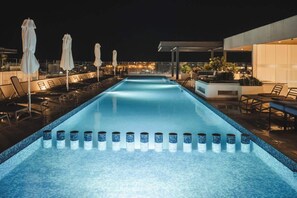 A nighttime swimming pool with lounge chairs and umbrellas, surrounded by modern architecture. - Stylish Rooftop Condo w Ocean Views and Pools (Playa del Carmen)