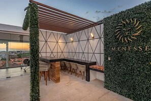 A rooftop bar with a geometric wall design, a wooden pergola, and a view of the cityscape. - Modern Studio with Rooftop Pool & Ocean-View Gym (Playa del Carmen)