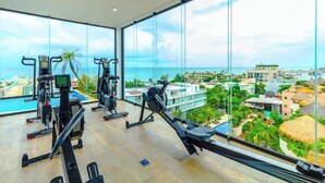 Ein Fitnessstudio mit unterschiedlichen Trainingsgeräten, großen Fenstern und Blick auf ein Küstenresort.