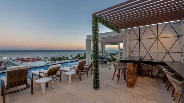 Eine Dachterrasse mit Pool, Liegestühlen und einer Bar mit Blick auf den Ozean.