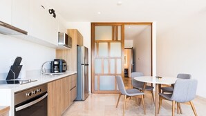 A modern kitchen with a stove, sink, and coffee maker. There is a dining area with a table and chairs. - Luxury 1BR Condo w Rooftop Pools and Ocean Views (Playa del Carmen)