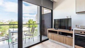 A modern kitchen with a large window, a flat-screen TV, and a dining area with chairs. - Luxury 1BR Condo w Rooftop Pools and Ocean Views (Playa del Carmen)