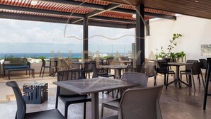An outdoor dining area with tables and chairs, a view of the ocean, and a covered section with a wooden ceiling. - Modern Condo Steps to 5th Ave and Beach w Rooftop Pool (Playa del Carmen)