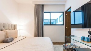 A hotel room with a bed, a desk, a chair, a TV, and a window. - Modern Condo Steps to 5th Ave and Beach w Rooftop Pool (Playa del Carmen)