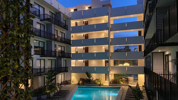 A multi-story hotel with a swimming pool, balconies, and outdoor seating. - Studio w Rooftop Pool Near Beach & 5th Ave (Playa del Carmen)
