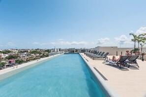 Une piscine sur le toit, dotée de chaises longues et offrant une vue sur le paysage urbain.