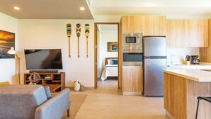 Una sala de estar moderna con un televisor de pantalla plana, un sofá y un comedor con armarios de madera y un refrigerador.