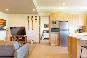 A modern living room with a flat-screen TV, a sofa, and a dining area with wooden cabinets and a refrigerator. - Mangrove View 2BR w Rooftop Pool Near 5th Ave (Playa del Carmen)