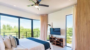 Un dormitorio con una cama grande, un ventilador de techo, un televisor y un balcón con vistas a la vegetación.