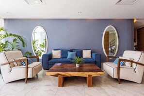 Un salón con un sofá azul, dos sillones, una mesa de centro de madera y dos espejos grandes en las paredes.