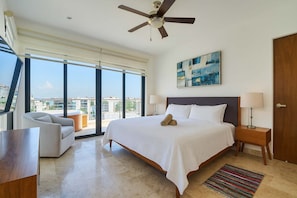 A modern hotel room with a large bed, a ceiling fan, a view of the city, and a balcony with a sofa. - Stylish Hideaway w Rooftop Jacuzzi, Pool and Gym (Playa del Carmen)