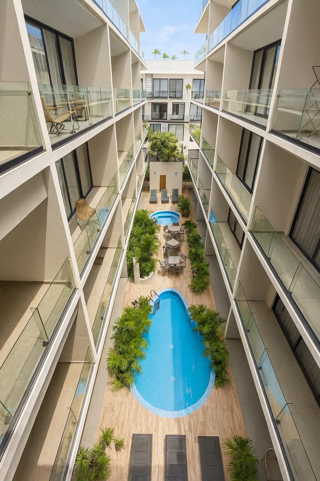 Um edifício moderno de vários andares com um pátio central, apresentando uma piscina, rodeado por vegetação e áreas de estar mobiliadas.