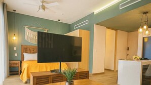Quarto de hotel moderno com uma cama grande, televisão de tela plana, mesa de centro de madeira e uma pequena área de trabalho.