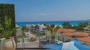 Ein Balkon mit Meerblick, einem Blumentopf und einer Sitzecke mit gestreiftem Kissen.