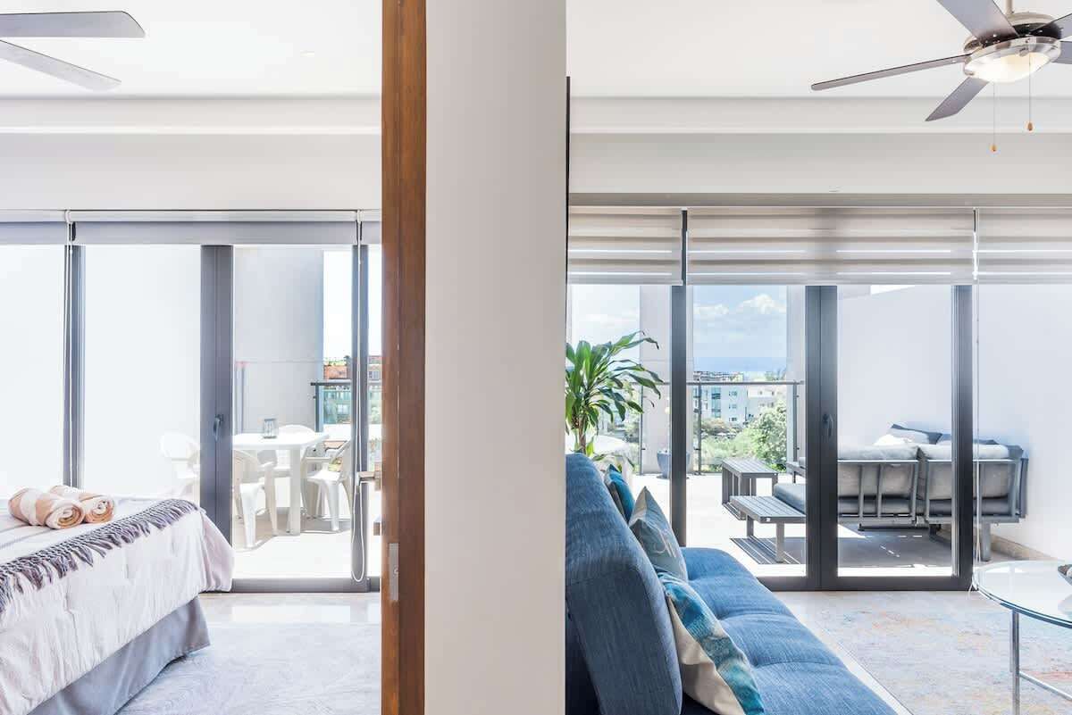A modern hotel room with a bed, a sofa, and a balcony with a table and chairs.