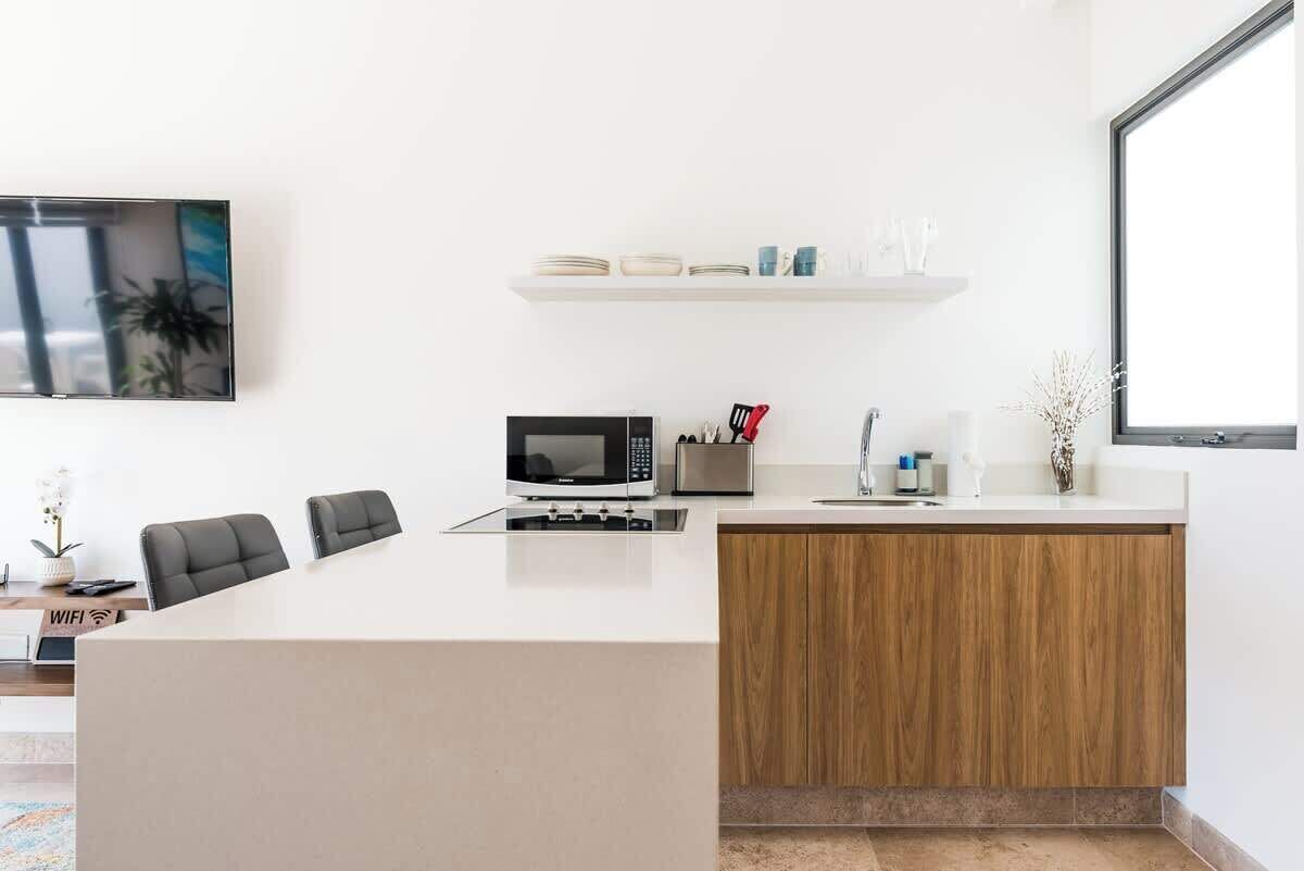 A modern kitchen with a microwave, sink, and wooden cabinets. There are two black chairs and a small table with a plant.
