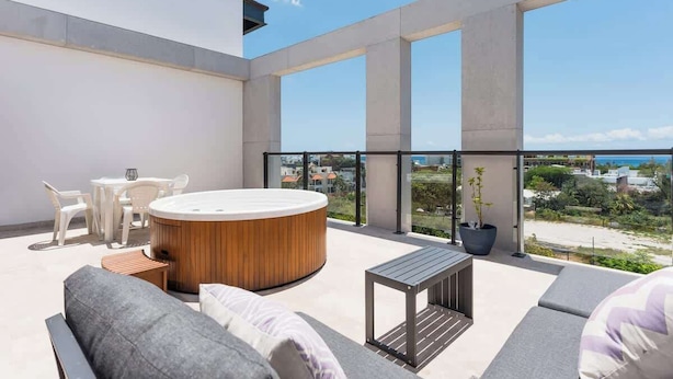 A modern outdoor balcony with a hot tub, seating, and a view of the beach. - Rooftop Pool and Private Hot Tub with Ocean Views (Playa del Carmen)