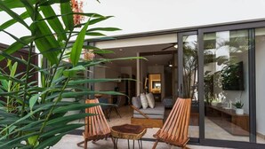 Un espacio al aire libre moderno con dos sillas de madera y una mesita, rodeado de exuberantes plantas verdes.