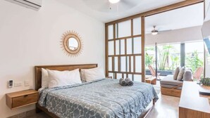 Un dormitorio con cama, mesita de noche y un ventanal con vistas a zonas verdes.
