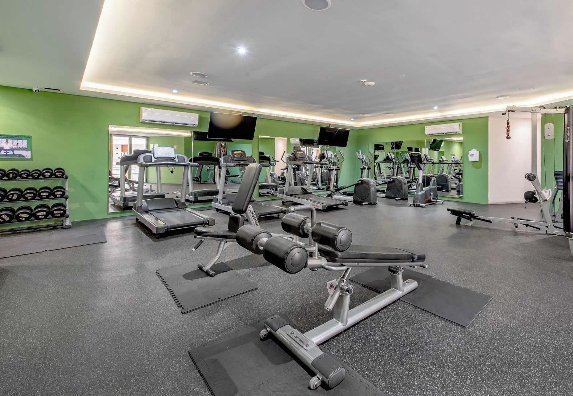 Una palestra con tapis roulant, macchinari per pesi e manubri.