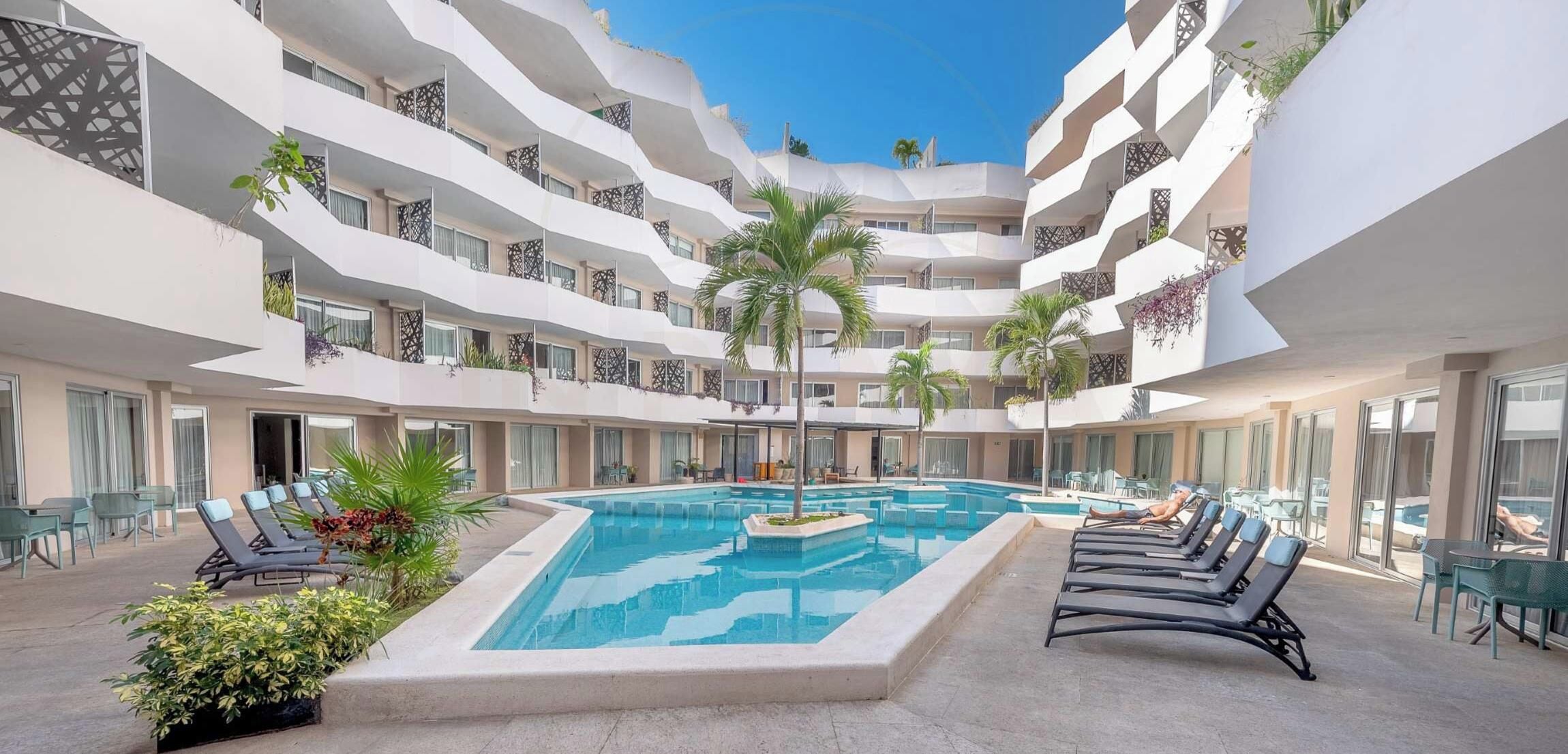 Un hotel de varios niveles con una piscina central, mobiliario exterior y balcones con plantas.