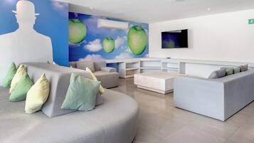 Un'area d'attesa moderna con un grande murale, posti a sedere e un televisore a parete.