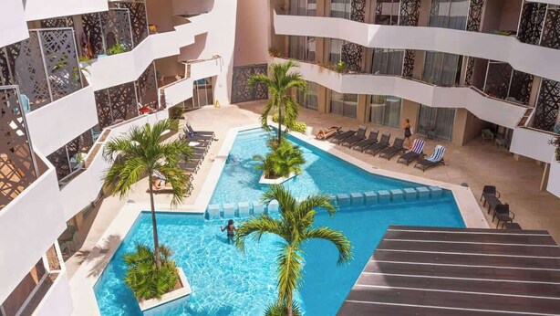 En pool inomhus med flera nivåer, palmer, solstolar och en modern arkitektonisk design.