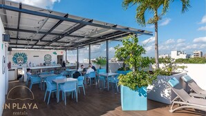 Ett utomhusområde med sittplatser, blå stolar och bord, en bar och en palm.